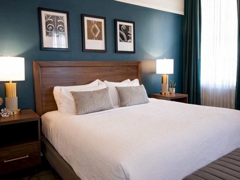 Hotel room with teal accent wall, wooden headboard, white bedding, and architectural artwork