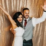 Bride and groom embracing with raised arms in gold sequin photo booth