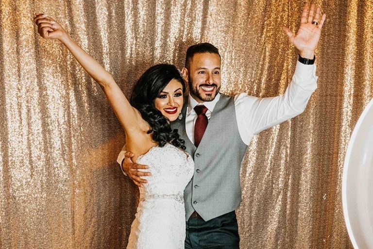 Bride and groom embracing with raised arms in gold sequin photo booth