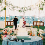 Three-tier wedding cake with vertical pleating, floral cascade decoration, and turquoise accents displayed at tent reception