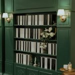 Dark green built-in bookshelf styled with neutral books, fresh white flowers, and vintage decorative objects
