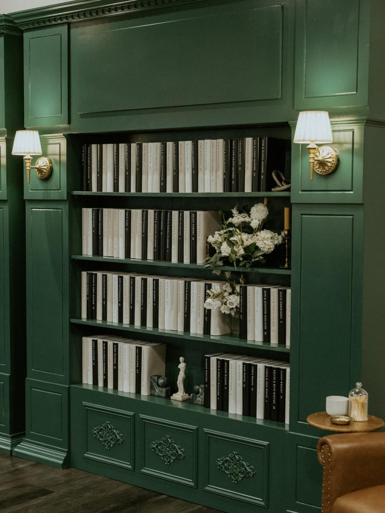 Dark green built-in bookshelf styled with neutral books, fresh white flowers, and vintage decorative objects
