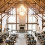 Rustic barn wedding reception with exposed beam ceiling, crystal chandeliers, and round tables with black linens