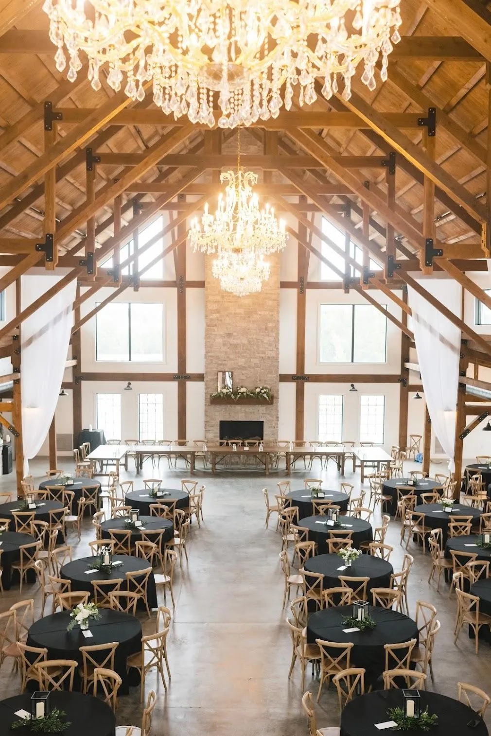 Rustic barn wedding reception with exposed beam ceiling, crystal chandeliers, and round tables with black linens