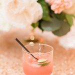 Pink ombré cocktail garnished with cucumber and mint beside peach-colored flowers