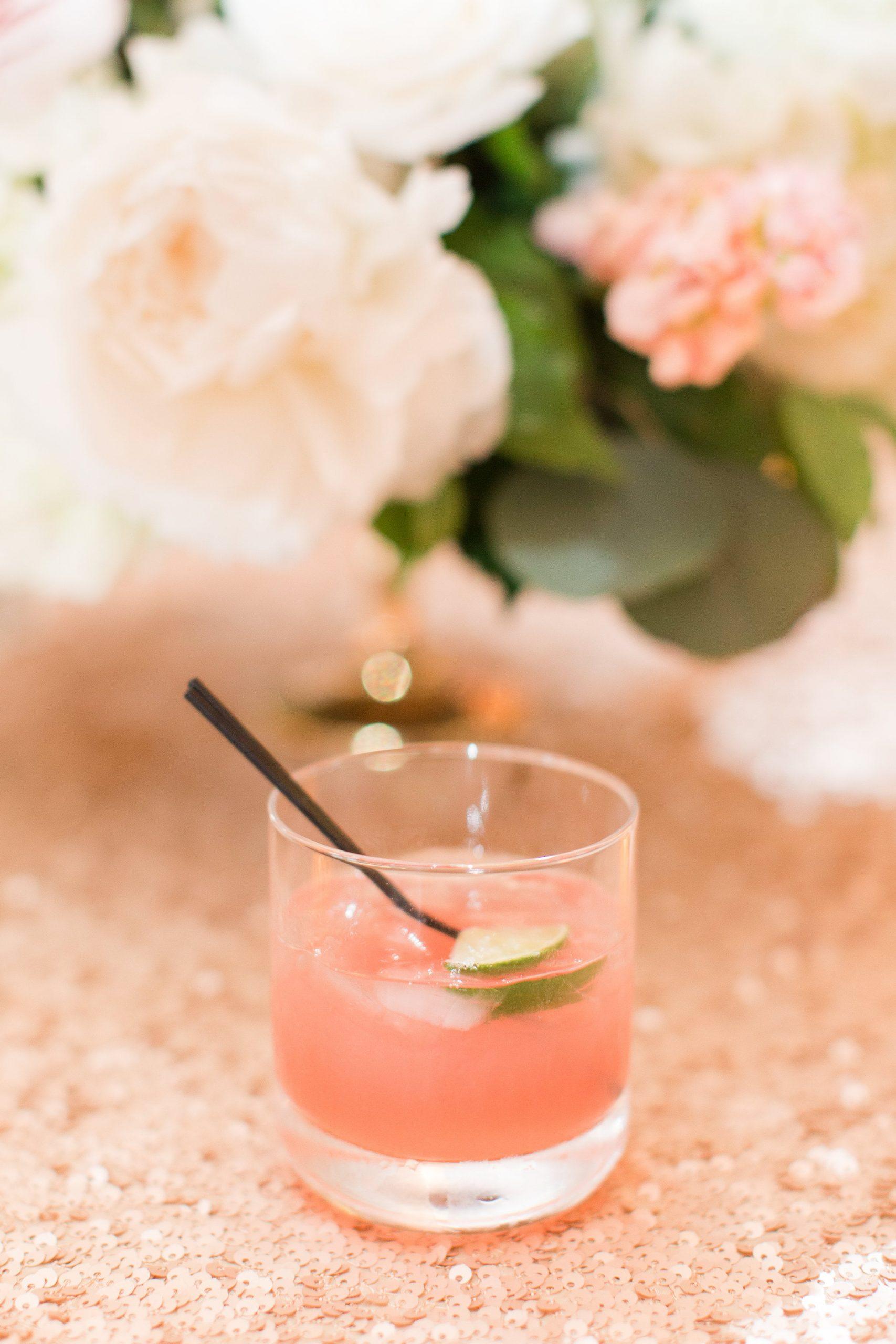 Pink ombré cocktail garnished with cucumber and mint beside peach-colored flowers