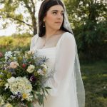 Bride outdoors holding white and green bouquet with veil and elegant makeup