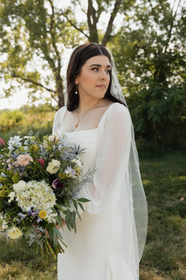 Bride outdoors holding white and green bouquet with veil and elegant makeup