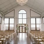 Industrial wedding ceremony space with arched windows, crystal chandelier, and gold chiavari chairs