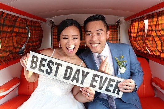 Newlyweds inside vintage van holding "BEST DAY EVER" sign and smiling at camera