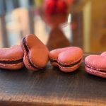 Five pink and brown macarons arranged on dark wooden surface with blurred background