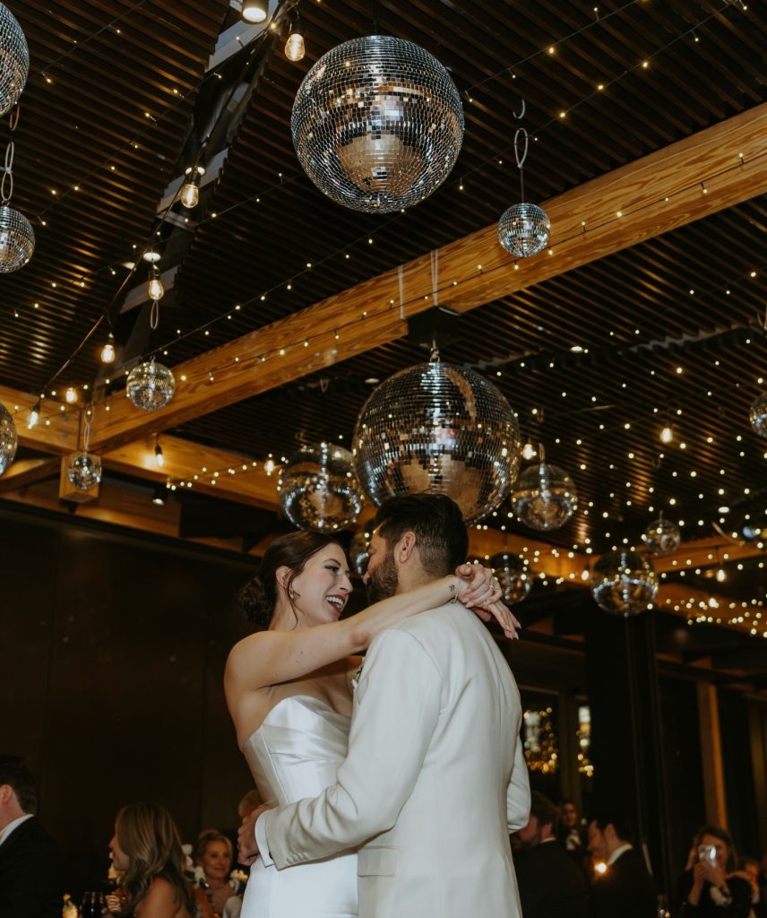 Newlywed couple dancing under disco balls and string lights at elegant wedding reception