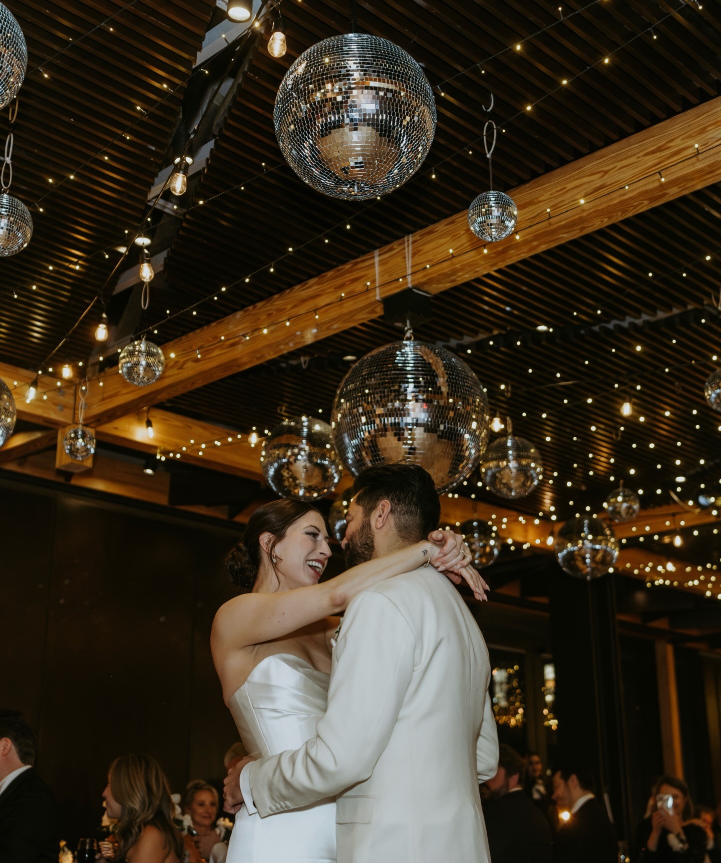 Newlywed couple dancing under disco balls and string lights at elegant wedding reception