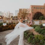 Bride in flowing white gown twirling outdoors on rooftop terrace with greenery