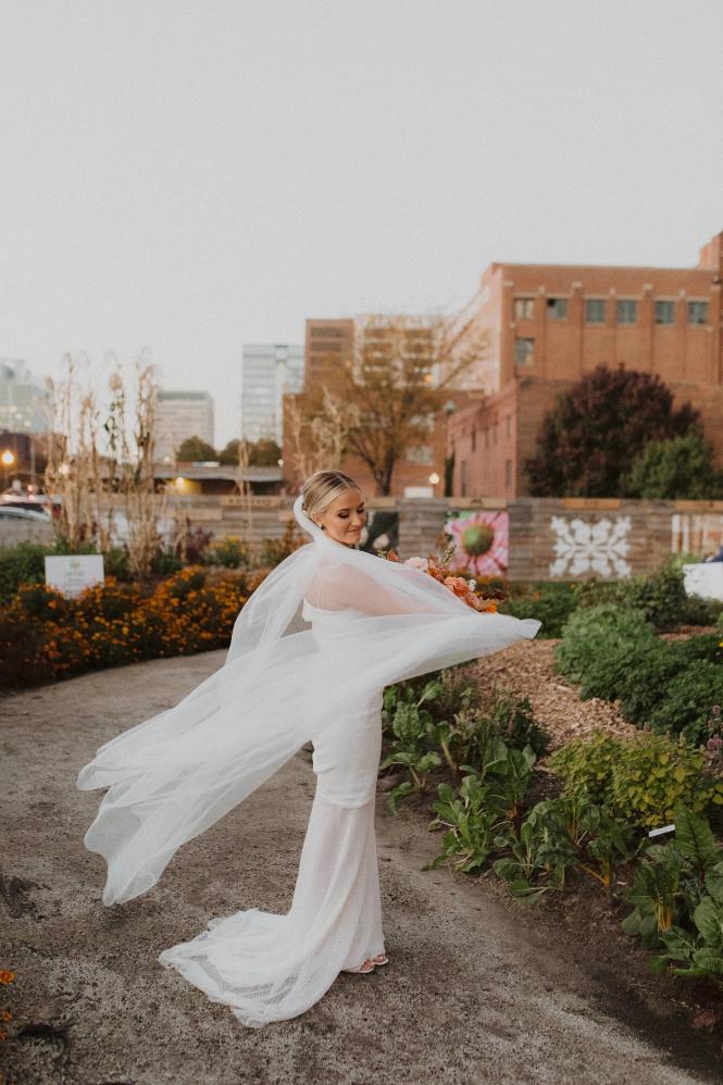 Bride in flowing white gown twirling outdoors on rooftop terrace with greenery