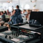 DJ equipment setup with laptop and controller at wedding reception, guests visible in blurred background