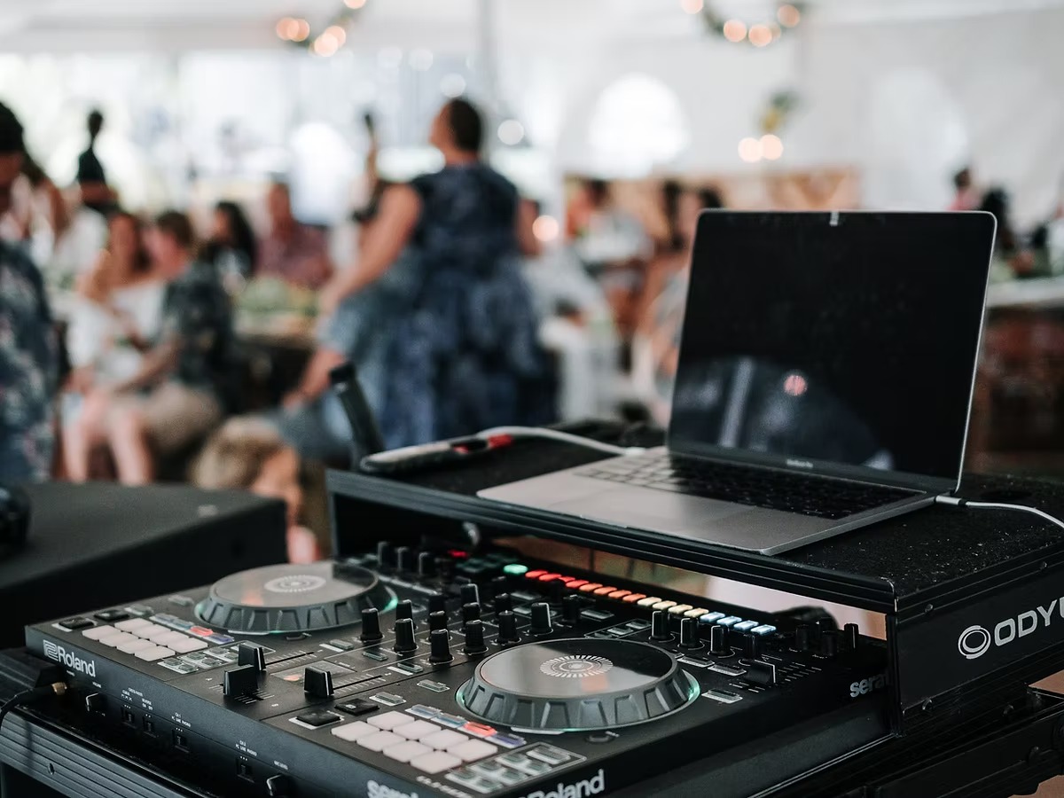 DJ equipment setup with laptop and controller at wedding reception, guests visible in blurred background