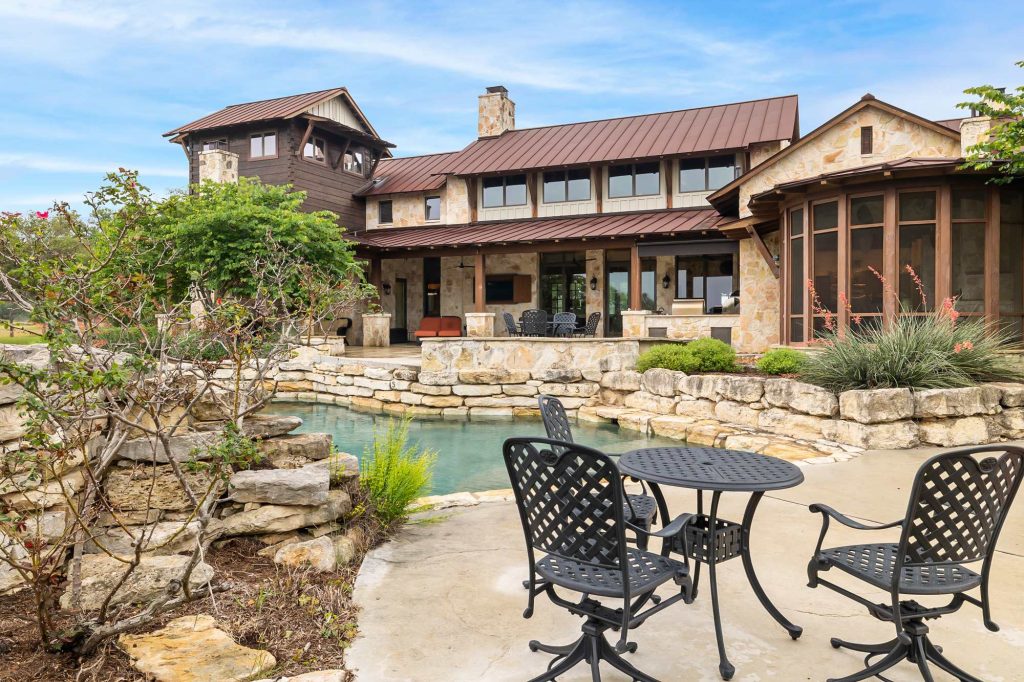 Texas Hill Country estate with stone exterior, metal roof, and backyard pool