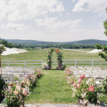 Outdoor wedding ceremony with floral arch and white chairs overlooking mountain landscape
