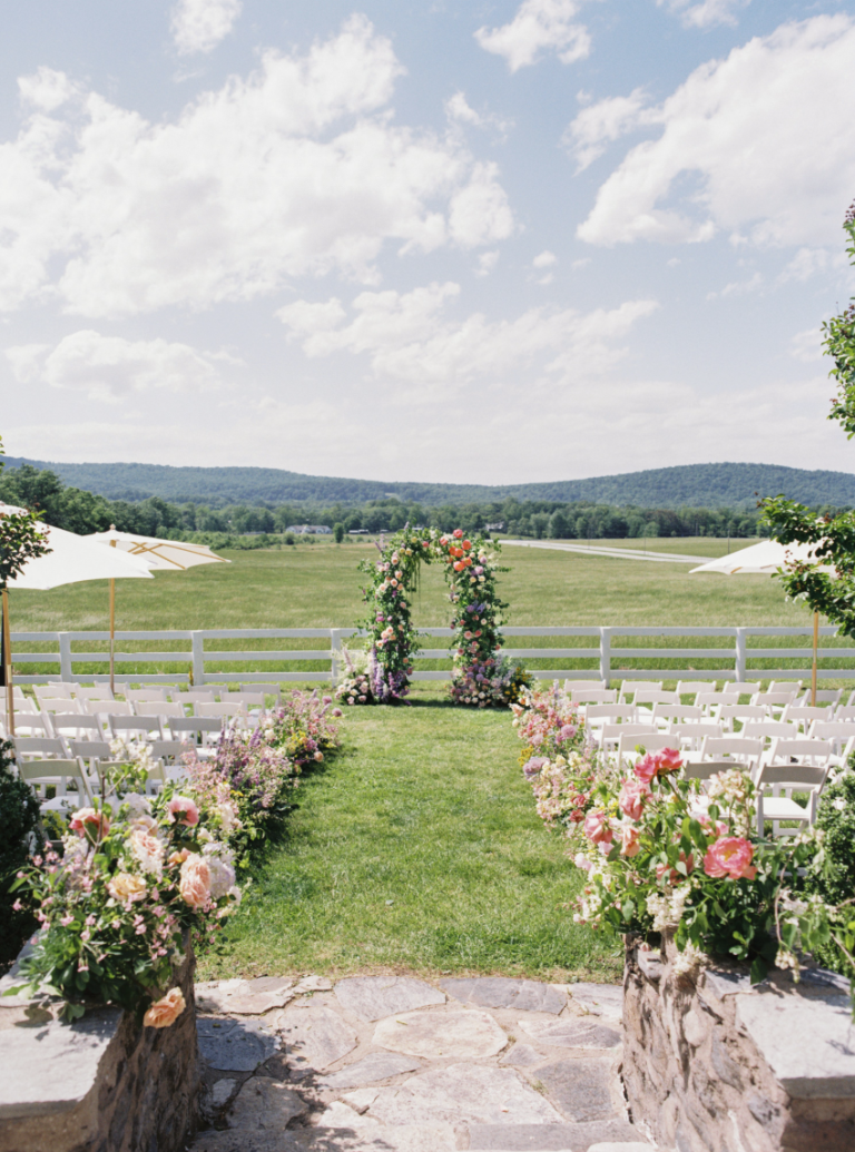 Outdoor wedding ceremony with floral arch and white chairs overlooking mountain landscape
