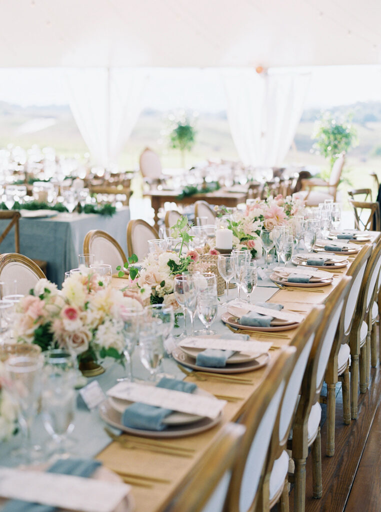 Outdoor wedding reception with mix of round and long tables featuring blue linens and white floral arrangements