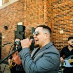 Male singer in gray suit performing with live band at outdoor wedding reception