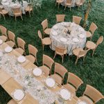 Outdoor wedding reception with cane-back chairs, round and rectangular tables adorned with floral runners and white place settings on green lawn