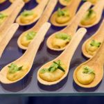 Rows of wooden appetizer spoons filled with creamy mousse and garnished with fresh herbs