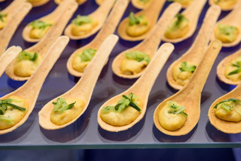 Rows of wooden appetizer spoons filled with creamy mousse and garnished with fresh herbs