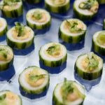 Cucumber rounds topped with cream cheese and herbs arranged on catering platter