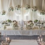 Luxurious Persian wedding ceremony table with tall floral centerpieces, crystal candelabras, ivory draping, and candlelit aisle