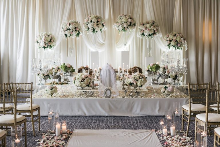 Luxurious Persian wedding ceremony table with tall floral centerpieces, crystal candelabras, ivory draping, and candlelit aisle