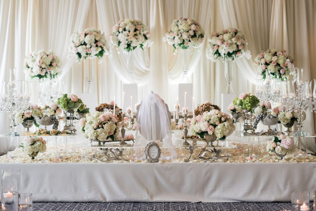 Luxury wedding reception table with tall pink and white floral centerpieces, draped backdrop, and crystal candelabras