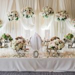 Luxury wedding reception table with tall pink and white floral centerpieces, draped backdrop, and crystal candelabras
