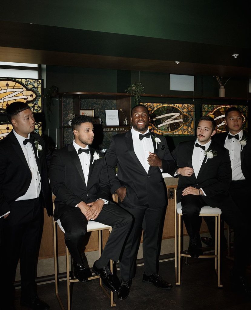 Groom laughs with groomsmen in black tuxedos at The Elliot's Art Deco-inspired bar area