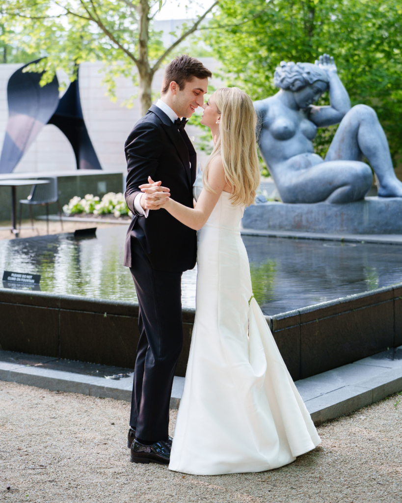 Marielle and Kyle embrace by fountain with sculpture in outdoor garden setting