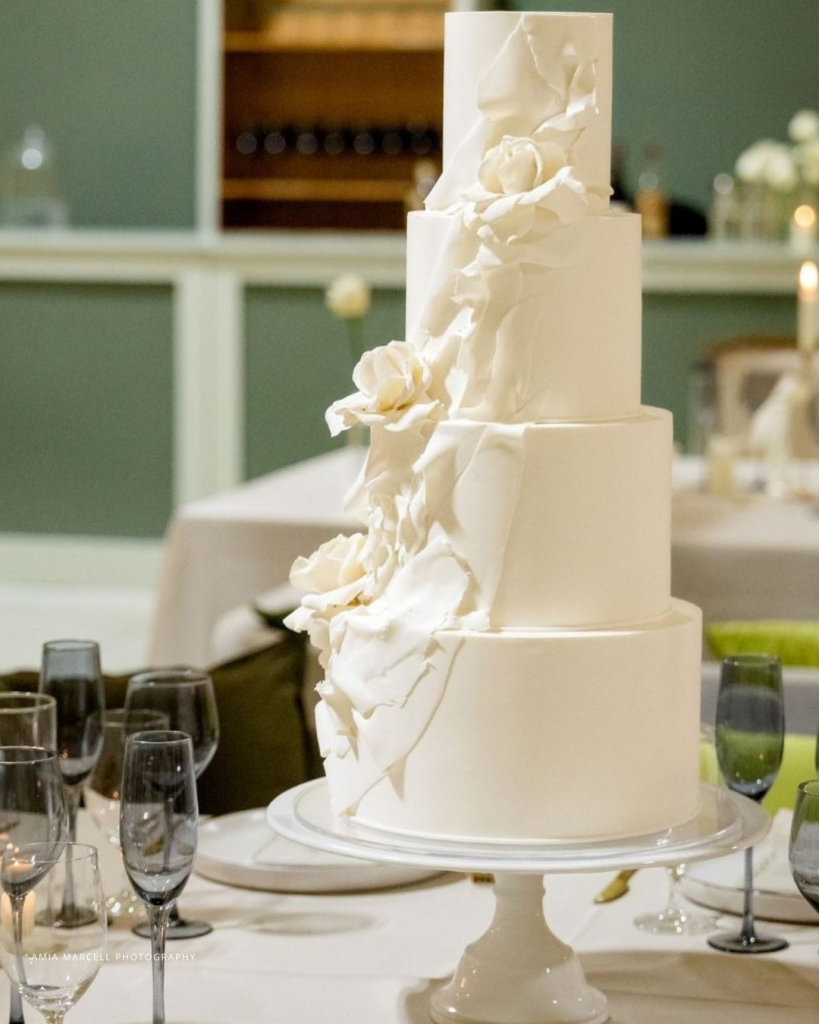 Four-tier white wedding cake with elegant ivory sugar flowers cascading diagonally across tiers