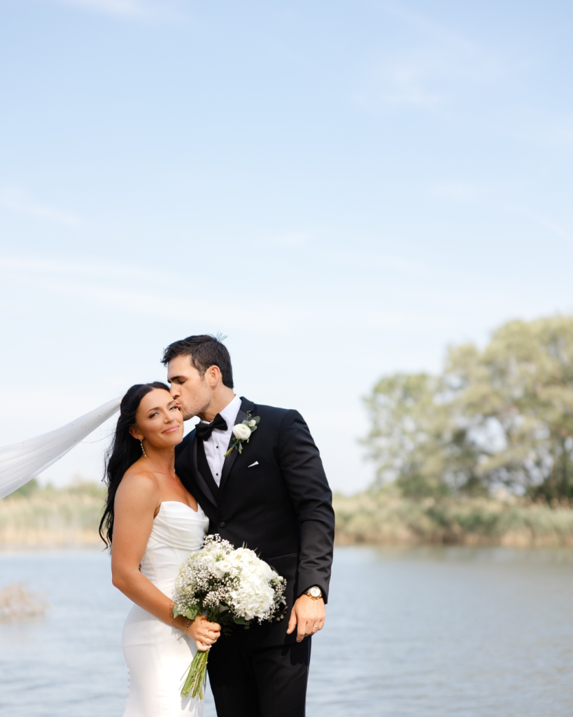 Hannah and Cole sharing intimate moment by lake with white floral bouquet