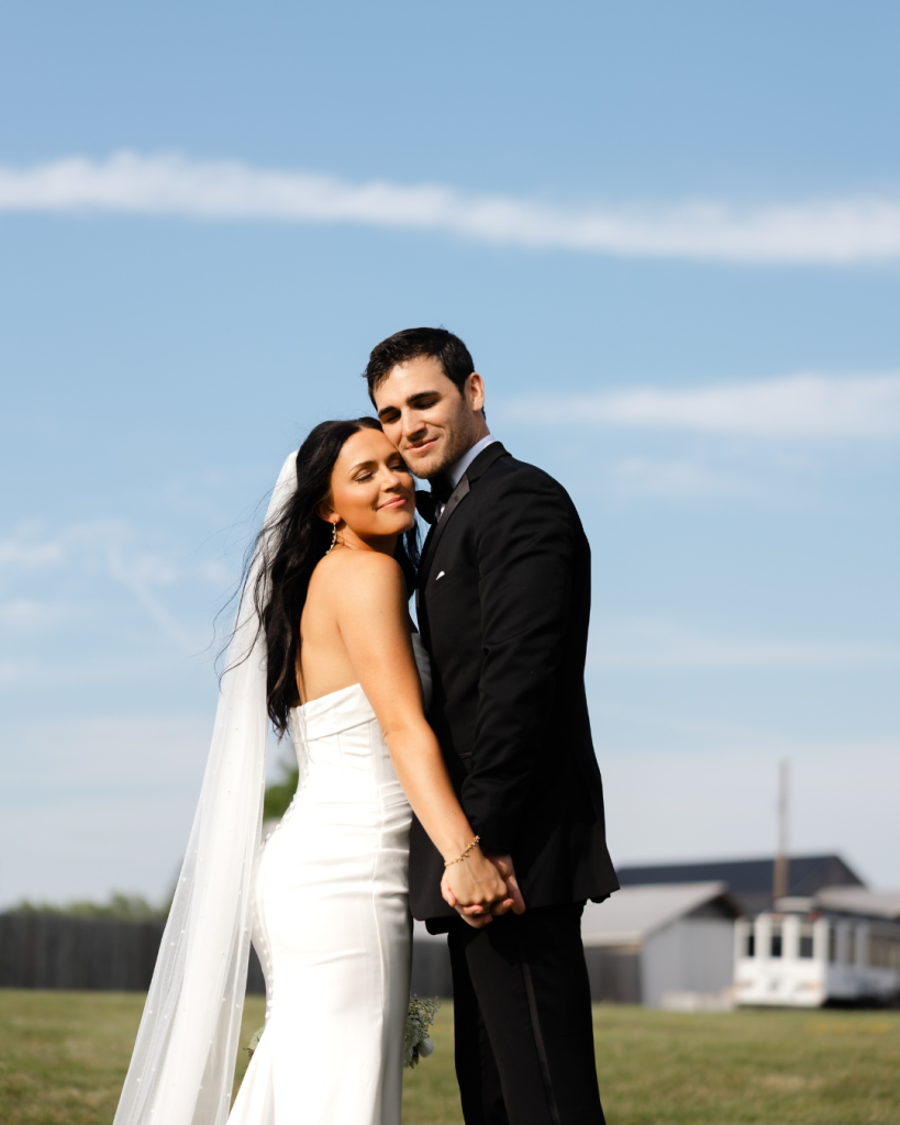 Hannah and Cole embracing in front of blue sky with rustic barn in background