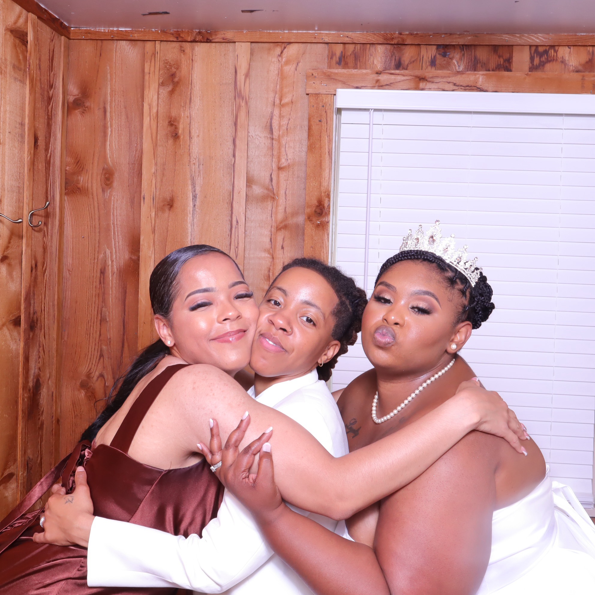 Three women embracing and smiling in a wedding photo booth, one wearing a tiara