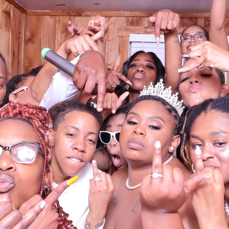 Large group of wedding guests celebrating with bride wearing tiara, making hand gestures at camera