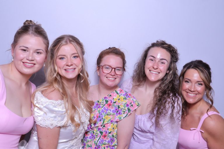 Bridesmaids in white dresses holding colorful bouquets in a photo booth