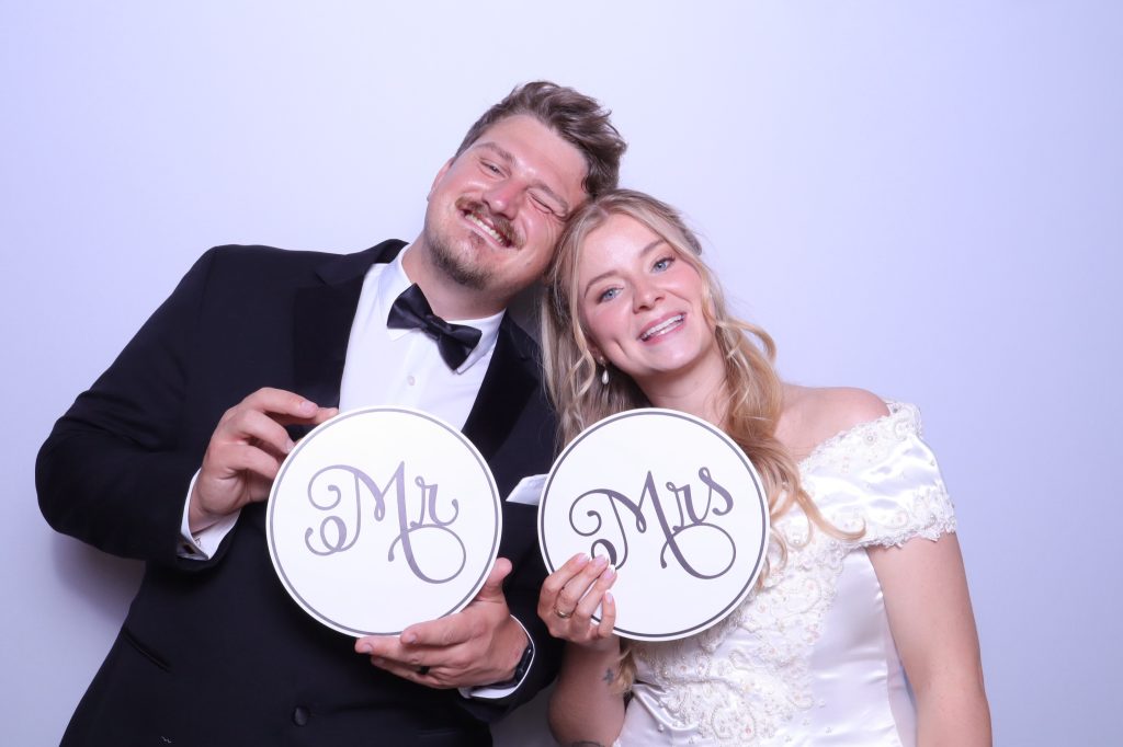 Newlywed couple holding "Mr" and "Mrs" signs at their wedding photo booth