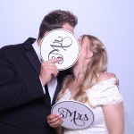 Bride and groom kissing behind Mr. and Mrs. photo booth props at their wedding reception