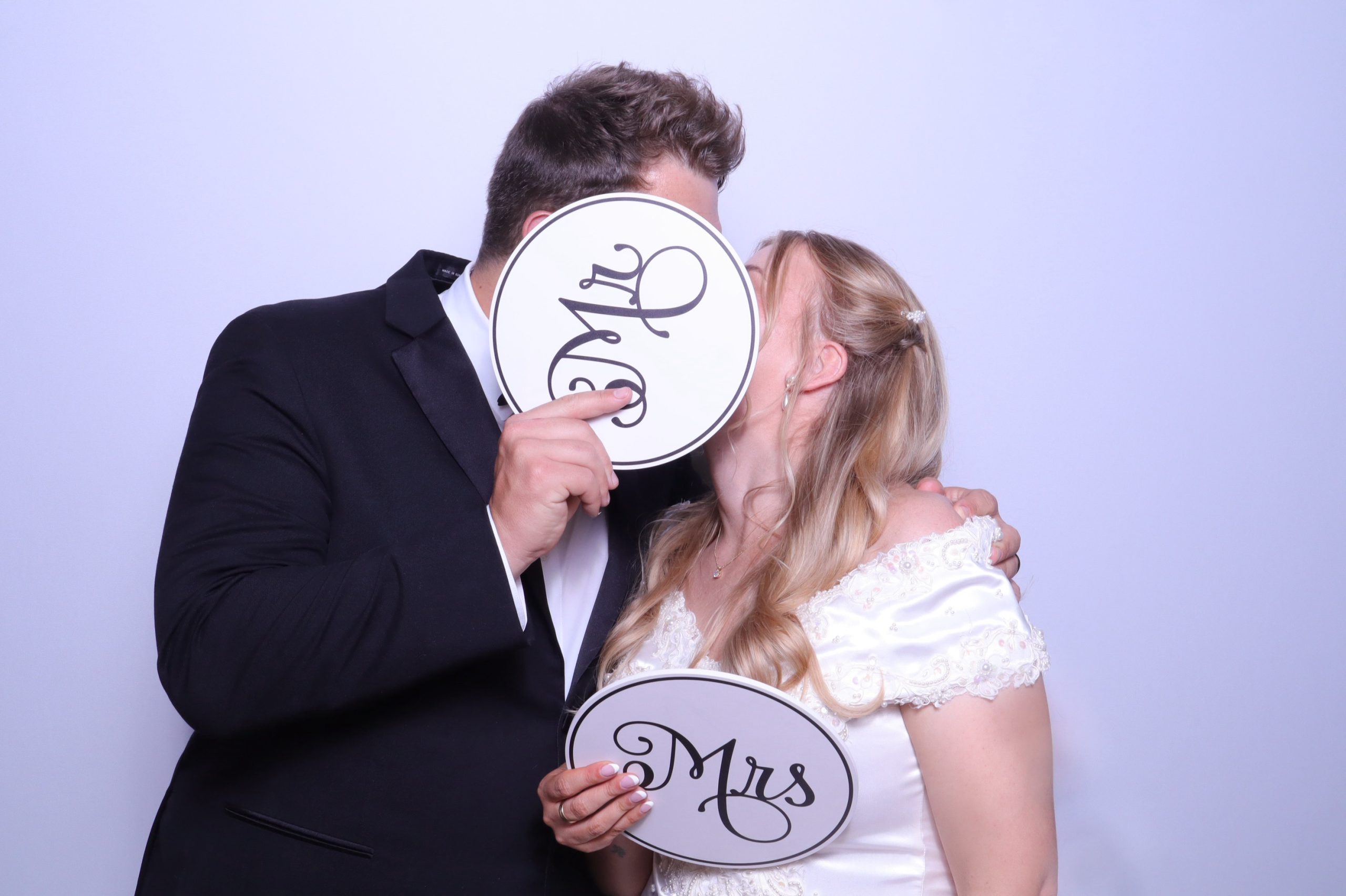 Bride and groom kissing behind Mr. and Mrs. photo booth props at their wedding reception