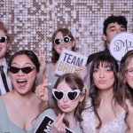 Wedding guests posing with fun props and sunglasses in front of shimmering sequin backdrop