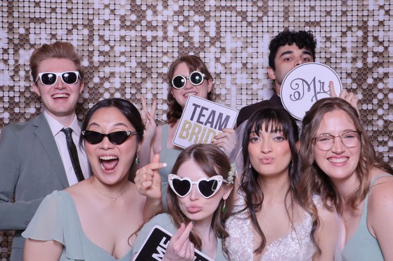 Wedding guests posing with fun props and sunglasses in front of shimmering sequin backdrop