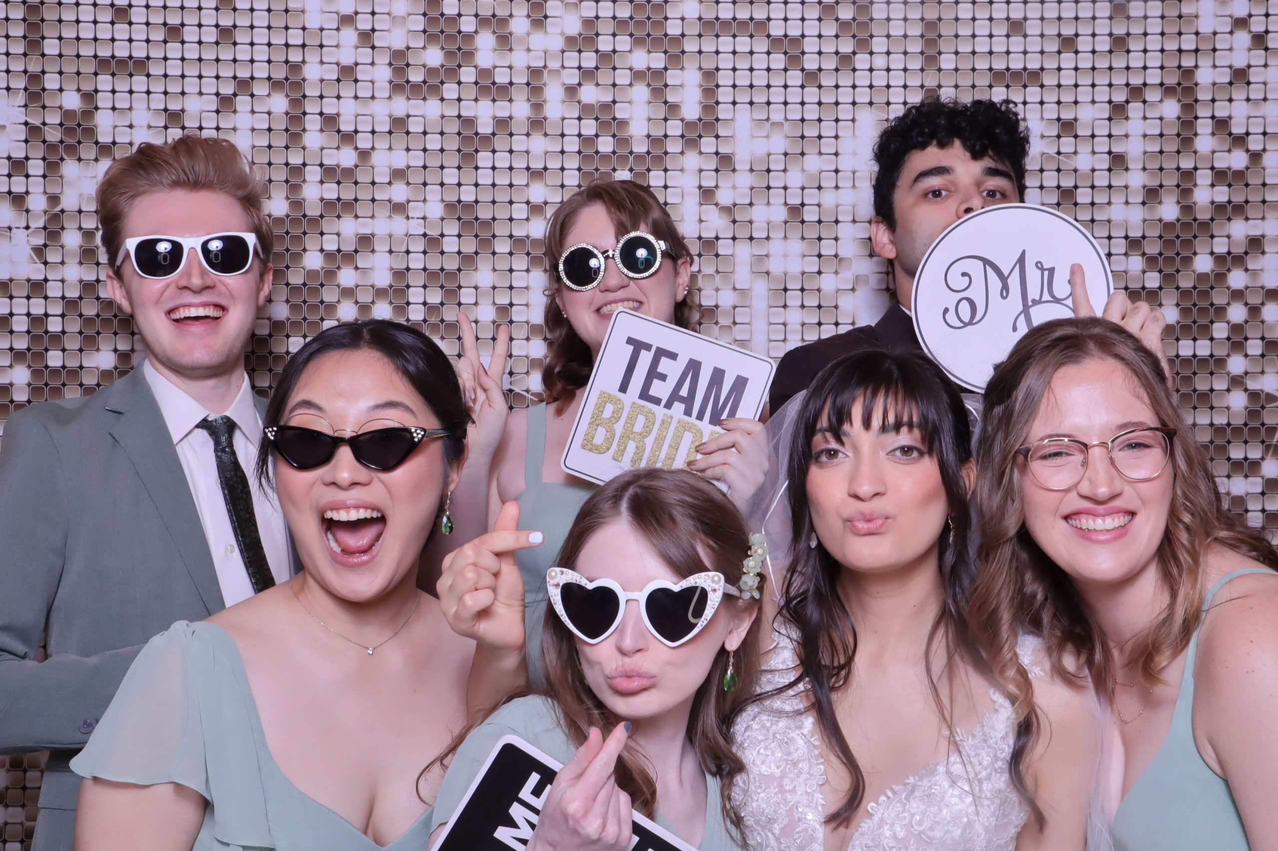 Wedding guests posing with fun props and sunglasses in front of shimmering sequin backdrop