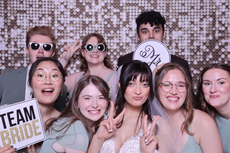Group of wedding guests posing together with props against sequin backdrop