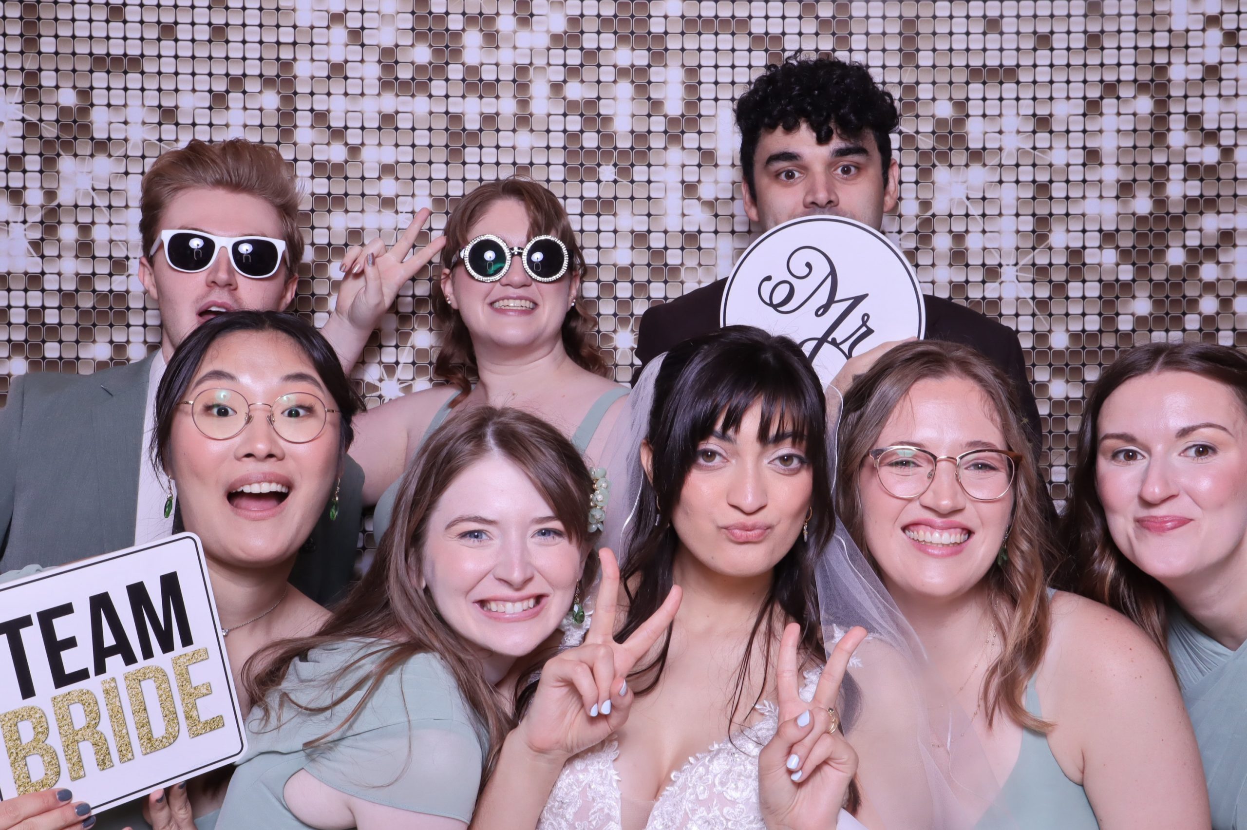 Group of wedding guests posing together with props against sequin backdrop